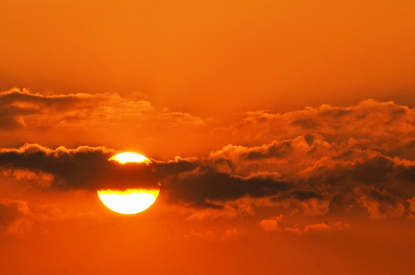 sun partially covered by clouds against orange sky