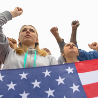 four youth protesting, U.S. flag in foreground