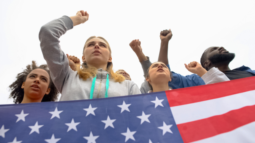 four youth protesting, U.S. flag in foreground