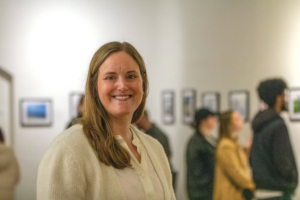 woman poses in art gallery as others in background view photos on the walls