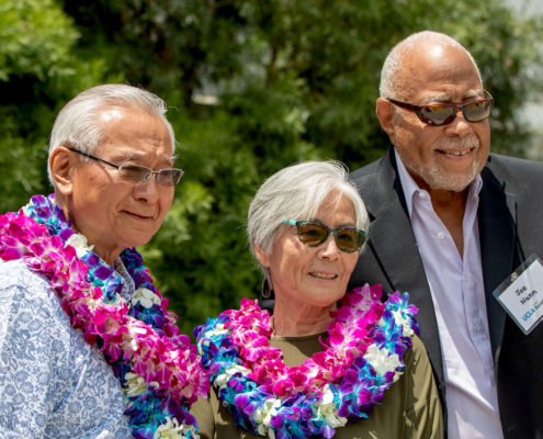 three people outdoors, two wearing leis