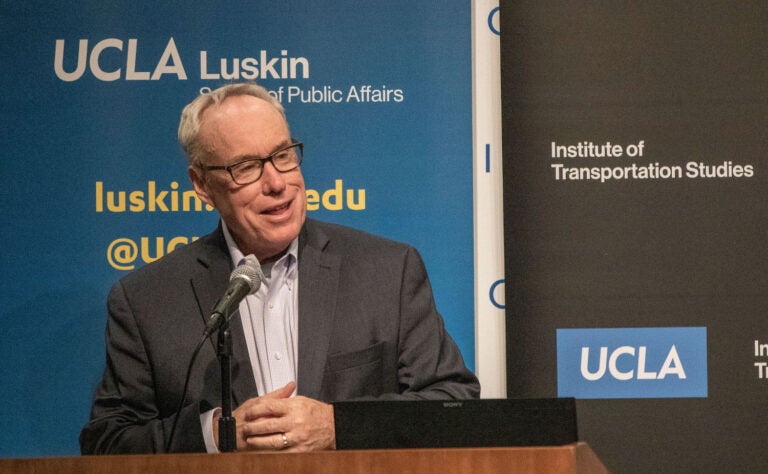 Man in glasses at podium with blue and black backdrop|