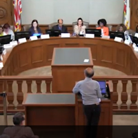 Man at podium addressing officials seated in semicircle