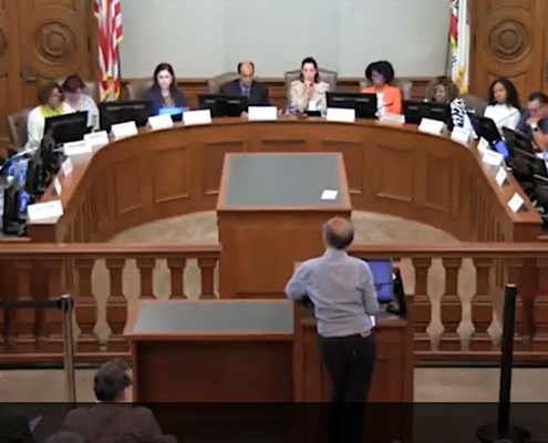 Man at podium addressing officials seated in semicircle