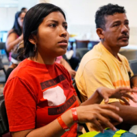 two adults and an infant sit in chairs at an orientation for new immigrants