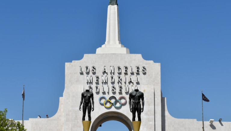 top of white building with spire and Olympic Games logo
