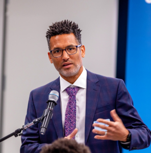 A man in a suit speaks at a podium