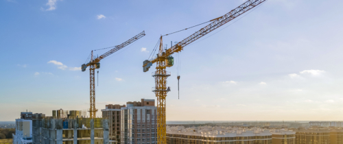 Cranes on the construction site surrounded by new real estates. Scenic aerial photo of growing city districts