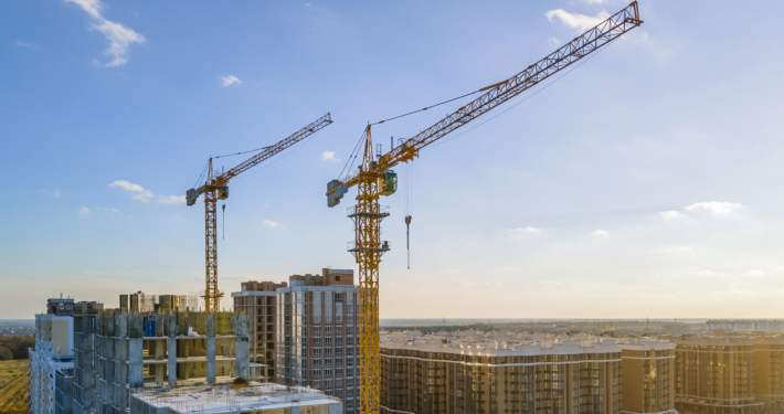 Cranes on the construction site surrounded by new real estates. Scenic aerial photo of growing city districts