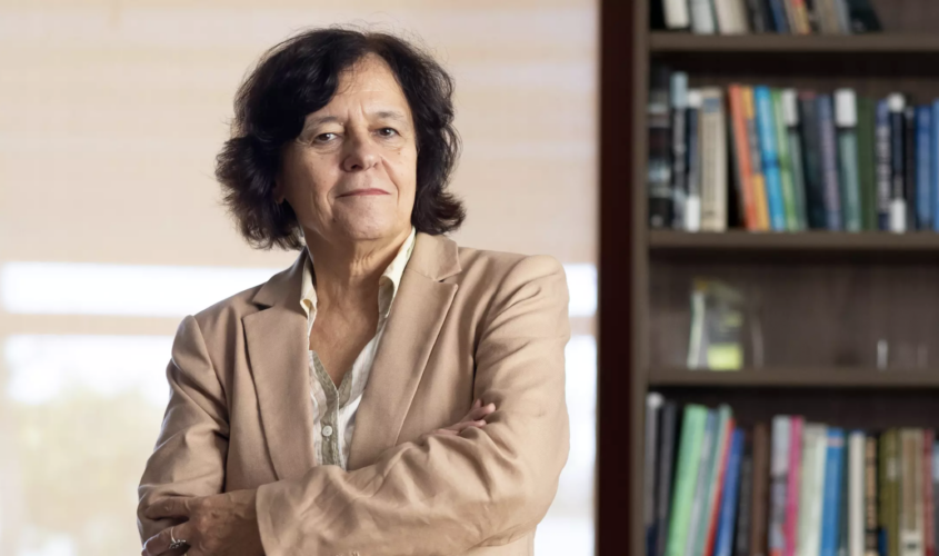 woman in tan suit next to bookcase