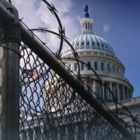 view of the U.S. Capitol Building at an angle behind razor wire fencing with clouds in the background.