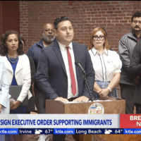 Mayor Karen Bass stands next to Edgar Garcia, MURP '06 who is at the pulpit introducing the mayor as she signs a new executive directive to protect immigrant communities amid ICE raids happening all across our city.