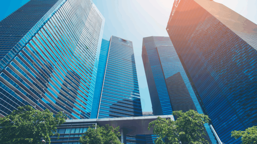 A photo of tall skycrapers coming a semi circle on a bright sunny day with the shadow of some of the building being cast on a few.