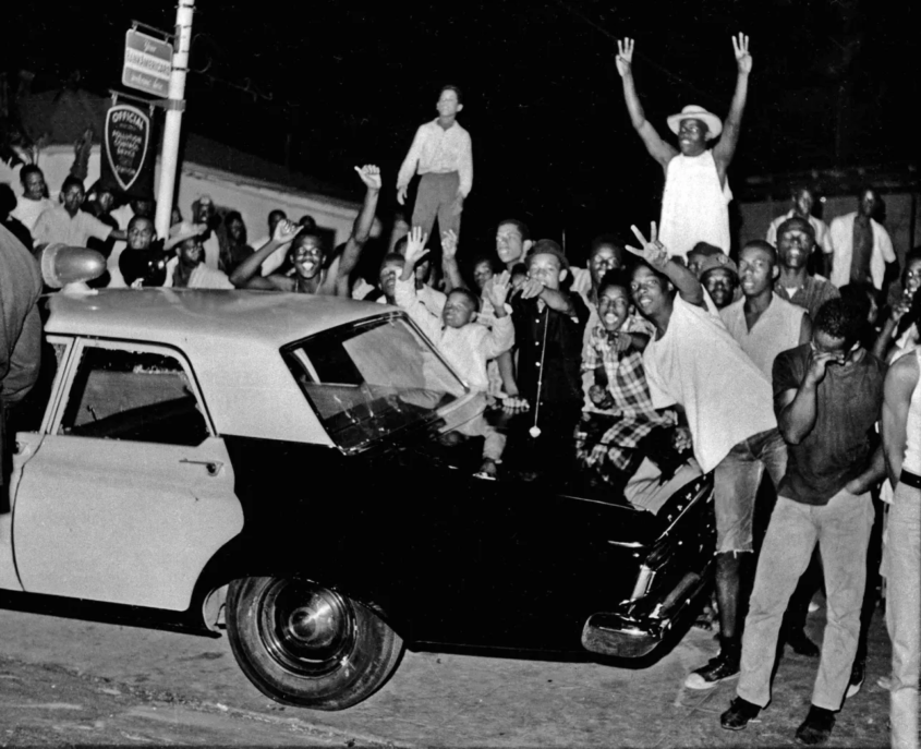 In this Aug. 12, 1965 file photo, demonstrators push against a police car after rioting erupted in the Watts district of Los Angeles. It began with a routine traffic stop 50 years ago this month, blossomed into a protest with the help of a rumor and escalated into the deadliest and most destructive riot Los Angeles had seen. The Watts riot broke out Aug. 11, 1965 and raged for most of a week. When the smoke cleared, 34 people were dead, more than a 1,000 were injured and some 600 buildings were damaged.