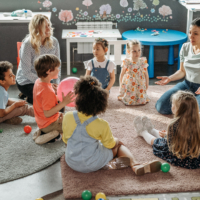 Canva – Kids with their Teacher Sitting on the Floor kids in a preschool sitting on the floor in a circle with a teacher