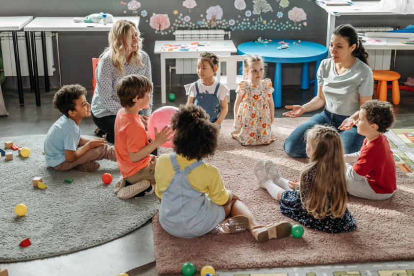 kids in a preschool sitting on the floor in a circle with a teacher