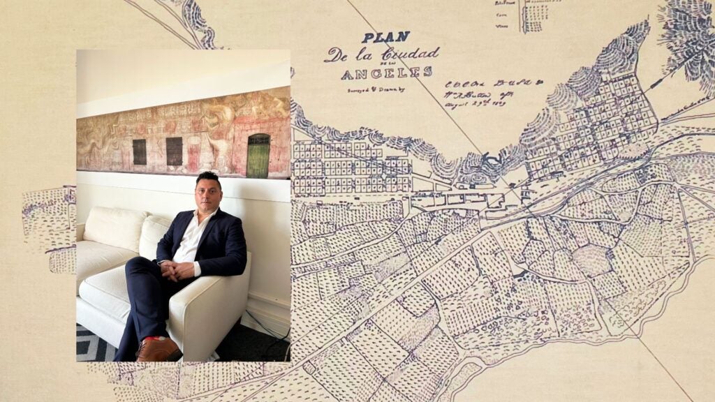Photo of Edgar Garcia sitting on a couch over a large map of Los Angeles.|||||Edgar Garcia sits behind a desk holding up a piece of paper with a black and white photo and words that say "A Mexican Street of Yesterday in a City of Today"||Edgar Garcia, Urban Planning alum, sits at a desk in his office holding up a photo map of El Pueblo de Los Angeles.