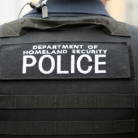 ICE Police Photo for Website Header Photo of a shoulder and back of a person wearing a bullet proof vest with the words Department of Homeland Security Police written across the back in white letters.