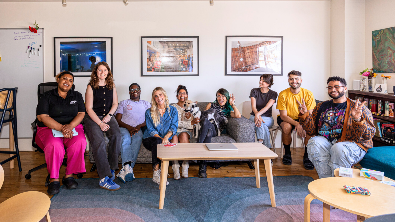 wide angle shot of a living room with people sitting across a couch on chairs facing the camera. theresa willmott-mcMahon sits on the side with her colleagues at her summer internship with Young People to the Front.|headshot of theresa willmott-mcmahon|Theresa stands in a room speaking in front of a group of colleagues at her summer internship.