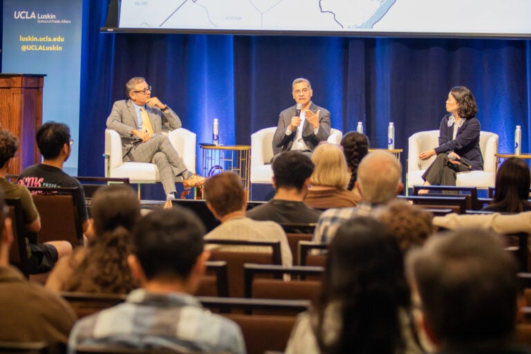 3 panelists speak in front of an audience on stage.|||