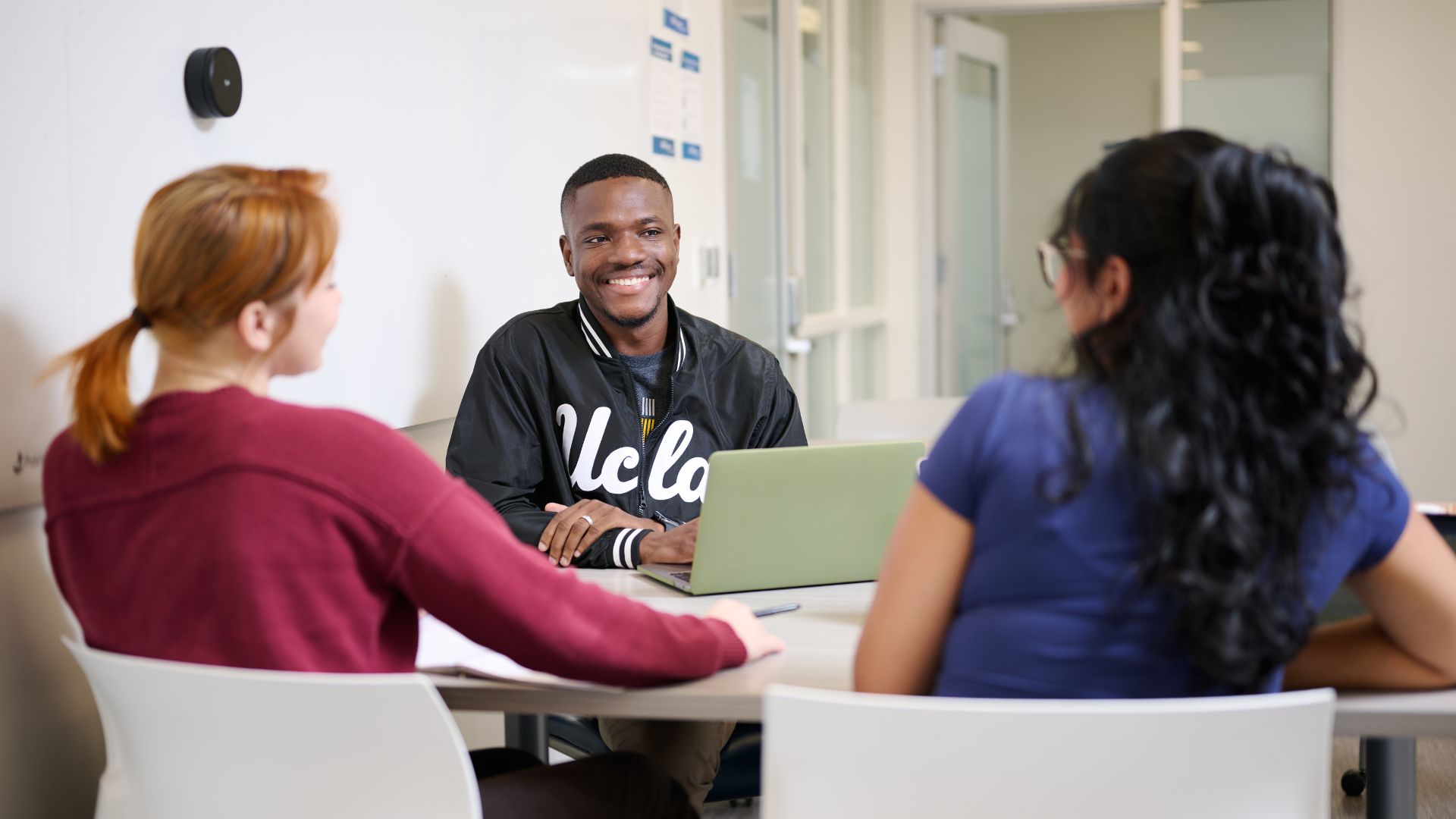 Prince Jarbo sits in the background at a conference table speaking to two friends in conversation.
