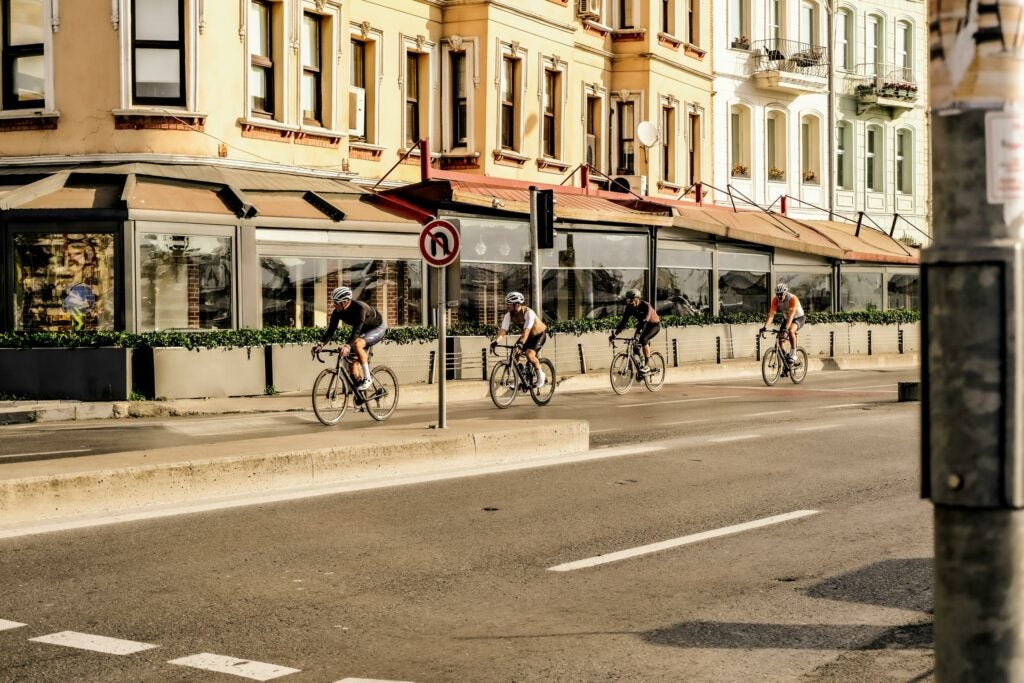 4 men biking cycling in a line on a street in a city