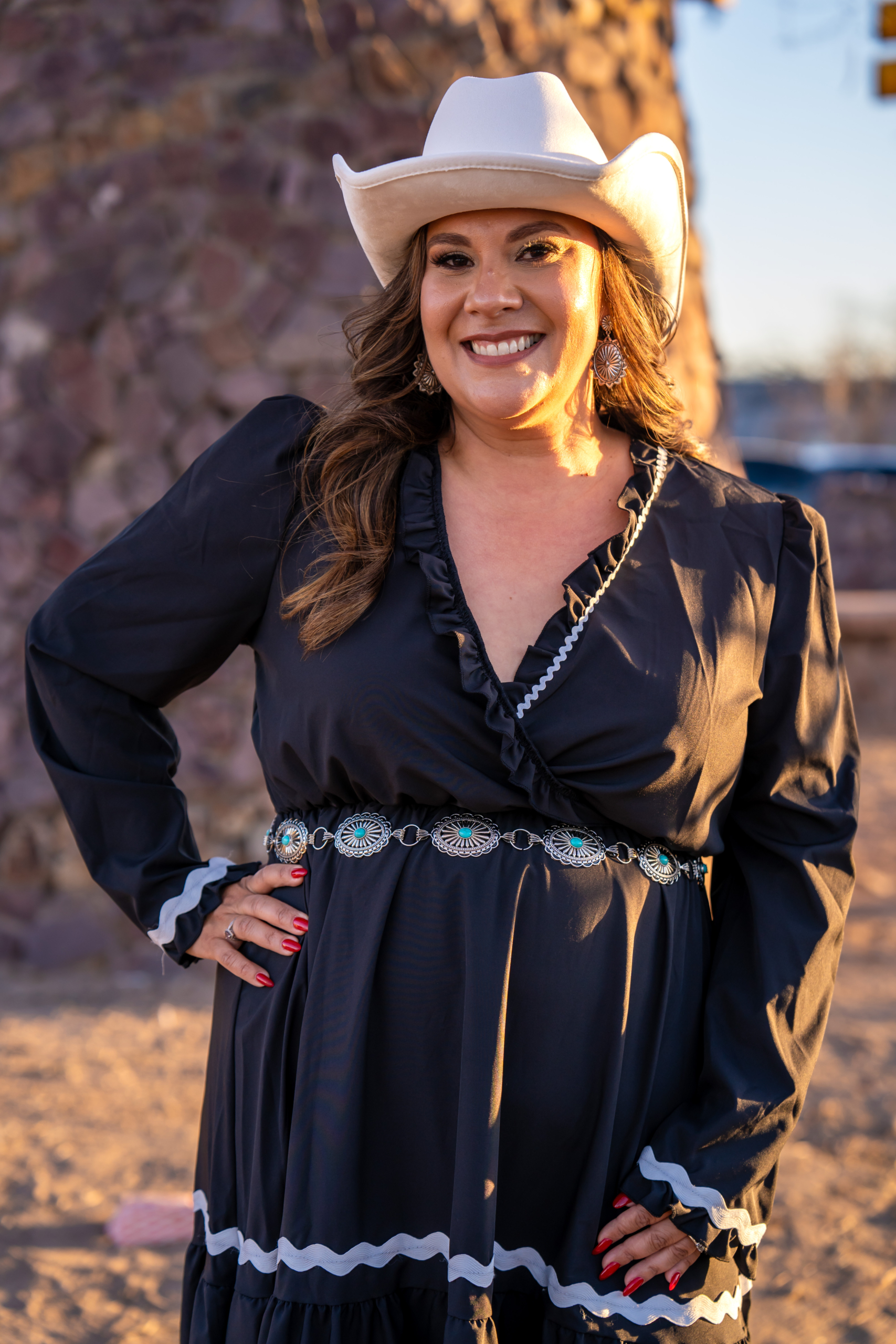 Selina Barajas with one hand on her hip, wearing a cowboy hat smiling at the camera. She is standing in a desert in Arizona. 