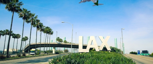 Photo of LAX sign with an airplane flying overhead at the los angeles airport.