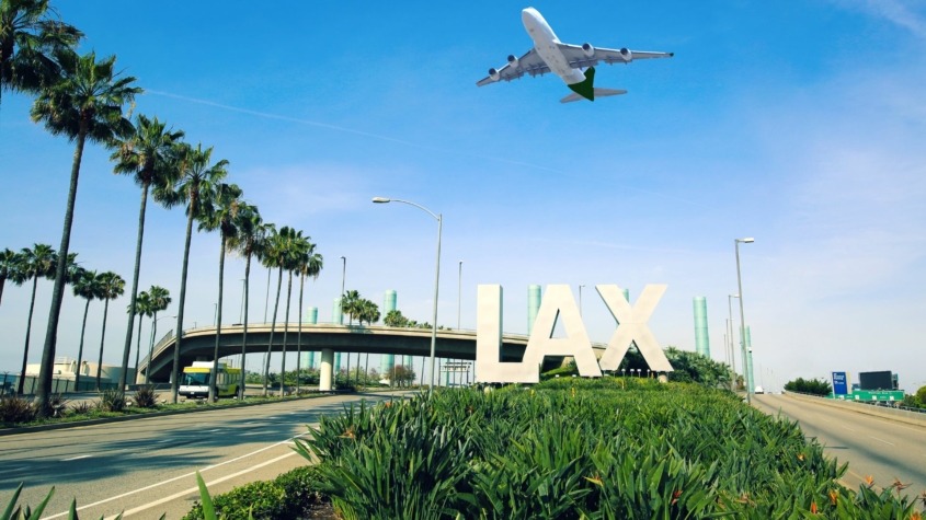 Photo of LAX sign with an airplane flying overhead at the los angeles airport.