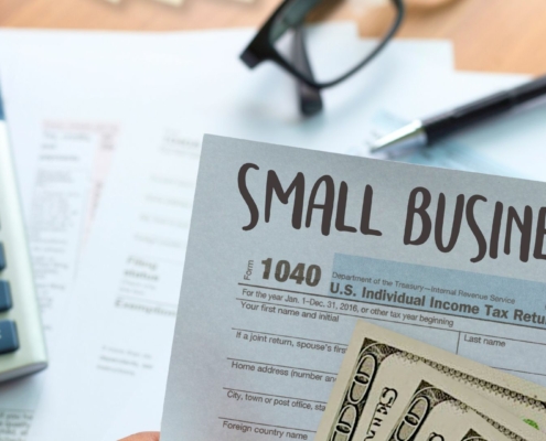 a photo of a hand holding a small business tax form with cash, and a calculator in the background