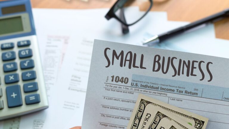a photo of a hand holding a small business tax form with cash, and a calculator in the background
