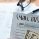 a photo of a hand holding a small business tax form with cash, and a calculator in the background