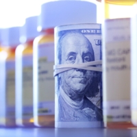 Roll Of One Hundred Dollar Bills In Row Of Prescription Medication Bottles A roll of one hundred dollar bills sits among a row of prescription medication bottles.