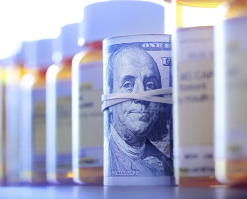 A roll of one hundred dollar bills sits among a row of prescription medication bottles.