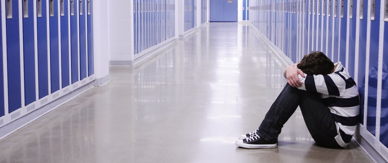 boy sitting with head in hands in school corridor amid blue lockers