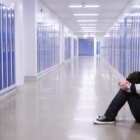 boy sitting with head in hands in school corridor amid blue lockers
