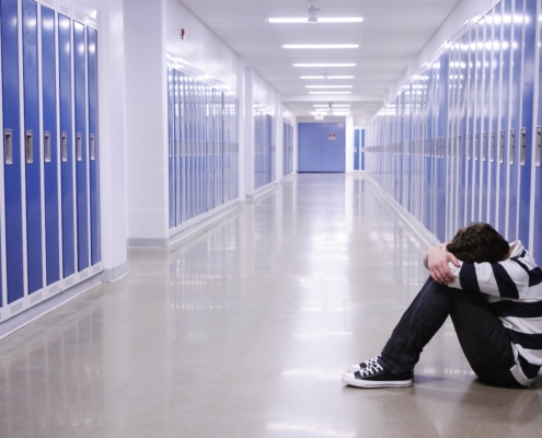 boy sitting with head in hands in school corridor amid blue lockers