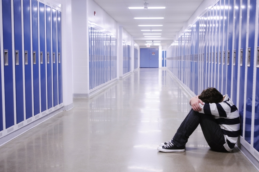 boy sitting with head in hands in school corridor amid blue lockers