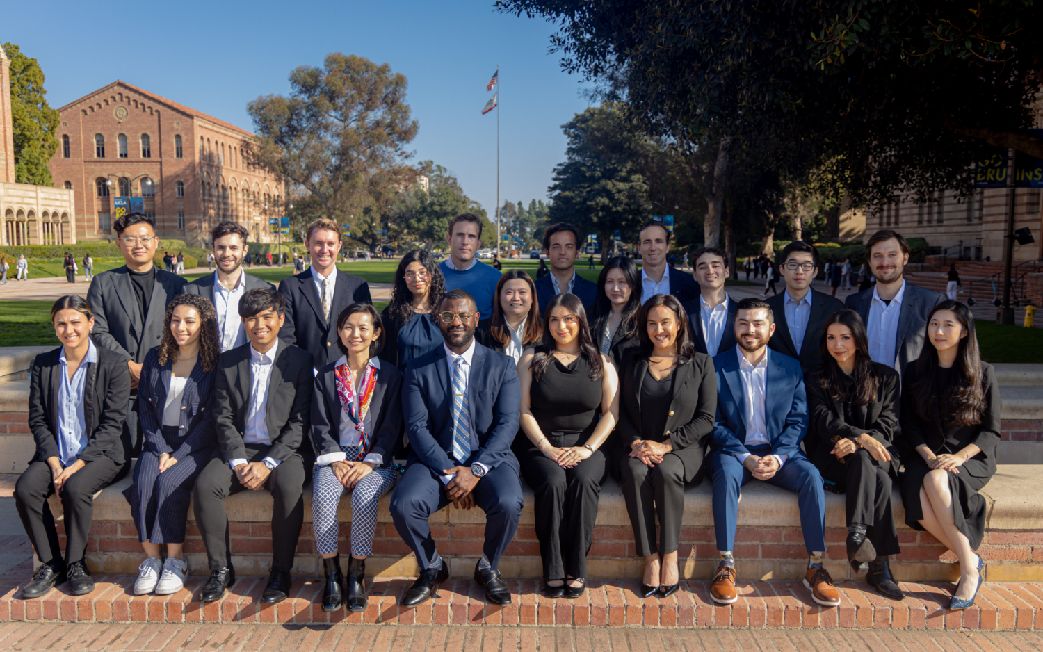 Cohort Pic Group of masters in real estate development students sitting in smiling in front of shapiro fountain in front of royce hall at ucla dressed professionally. there are 3 rows of them strategically posed for this group photo.