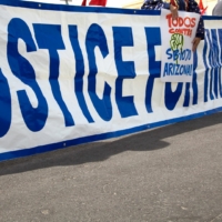 A group holds up a long sign that says Justice for Immigrants at a rally on the street.