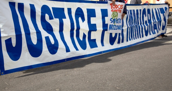 A group holds up a long sign that says Justice for Immigrants at a rally on the street.