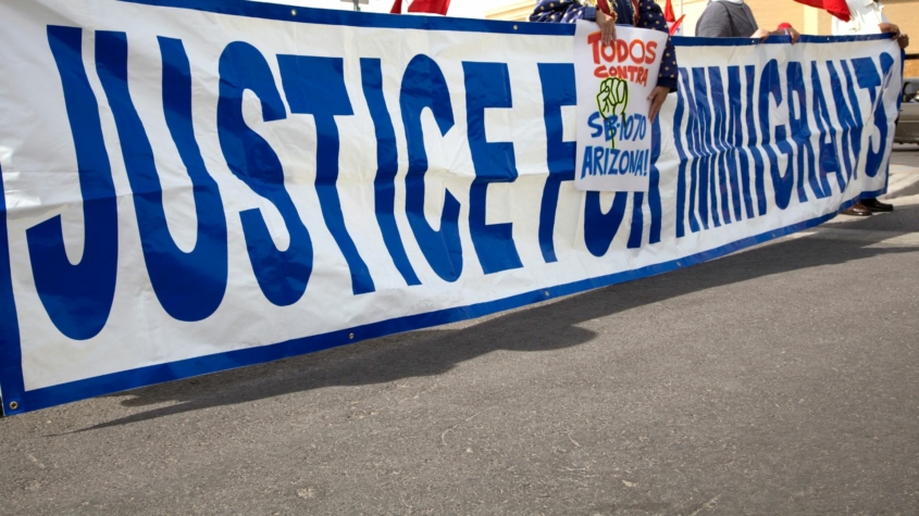 A group holds up a long sign that says Justice for Immigrants at a rally on the street.