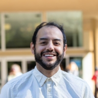Jose Loya stands smiling in front of the Public Affairs building at UCLA.