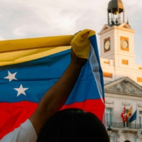 Photo of a man raising up the venezuelan flag in front of a political building in venezuela.