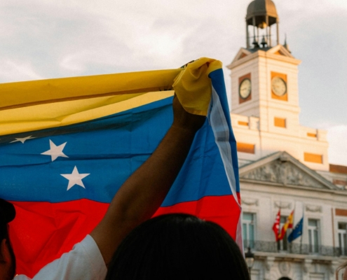 Photo of a man raising up the venezuelan flag in front of a political building in venezuela.