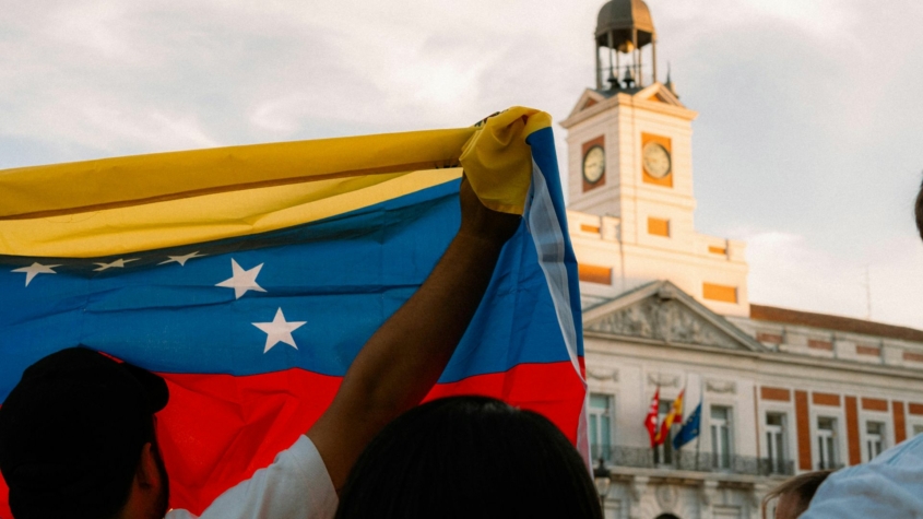 Photo of a man raising up the venezuelan flag in front of a political building in venezuela.
