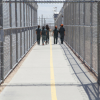 Group of people walking together in a fenced and gated ICE detention center.