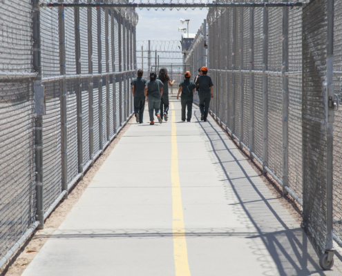 Group of people walking together in a fenced and gated ICE detention center.