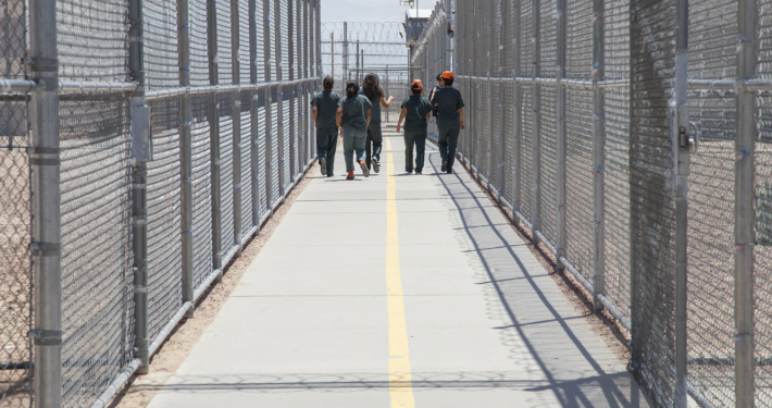 Group of people walking together in a fenced and gated ICE detention center.