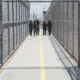 Group of people walking together in a fenced and gated ICE detention center.